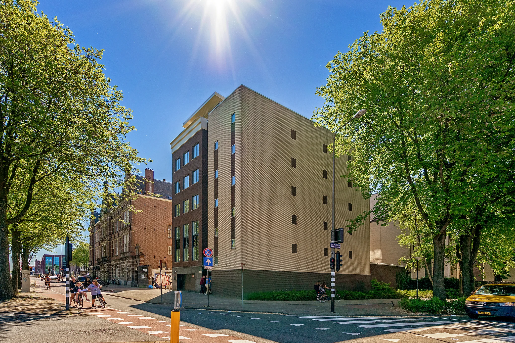 Moderne appartementen aan de Prins Hendrikkade in Amsterdam, omgeven door bomen en onder een stralende zon.